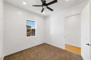 Carpeted spare room with ceiling fan and wood walls