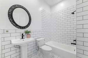 Bathroom featuring tiled shower / bath combo, toilet, and tile walls