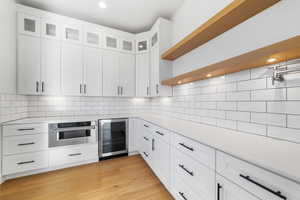 Kitchen featuring white cabinets, light hardwood / wood-style flooring, beverage cooler, and stainless steel oven