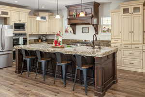 Kitchen featuring stainless steel appliances, dark hardwood / wood-style flooring, decorative light fixtures, cream cabinetry, and a center island with sink