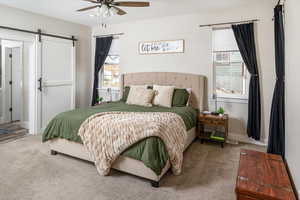 Bedroom featuring multiple windows, carpet, a barn door, and ceiling fan