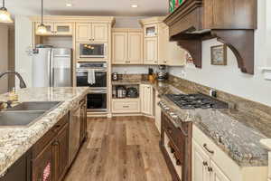 Kitchen with pendant lighting, sink, light hardwood / wood-style flooring, appliances with stainless steel finishes, and light stone counters