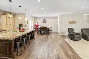 Kitchen featuring light stone countertops, light wood-type flooring, sink, pendant lighting, and cream cabinetry