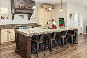 Kitchen with a large island with sink, dark stone countertops, dark hardwood / wood-style floors, and cream cabinetry