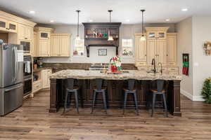 Kitchen with stainless steel appliances, an island with sink, pendant lighting, cream cabinetry, and hardwood / wood-style flooring