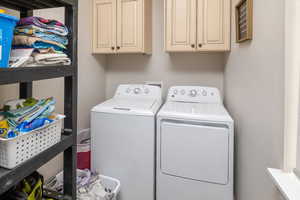 Clothes washing area featuring washing machine and clothes dryer and cabinets