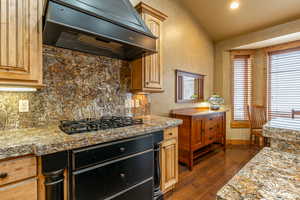 Kitchen with backsplash, premium range hood, light stone counters, black gas cooktop, and dark hardwood / wood-style floors