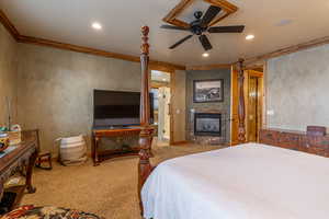 Carpeted bedroom featuring ceiling fan, crown molding, and a tile fireplace