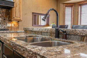 Kitchen featuring ventilation hood, dark stone countertops, and sink