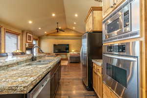 Kitchen with appliances with stainless steel finishes, dark hardwood / wood-style flooring, vaulted ceiling, ceiling fan, and sink