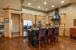 Kitchen with dark hardwood / wood-style floors, stainless steel appliances, premium range hood, and a kitchen island with sink