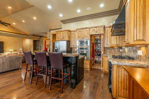 Kitchen with dark wood-type flooring, premium range hood, lofted ceiling, a center island with sink, and appliances with stainless steel finishes