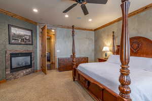 Carpeted bedroom featuring ceiling fan, crown molding, and a tile fireplace