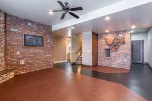 Unfurnished living room featuring a textured ceiling, ceiling fan, brick wall, and dark hardwood / wood-style floors