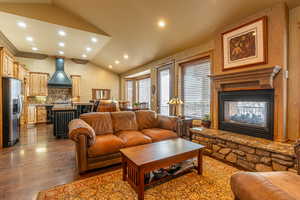 Living room with dark hardwood / wood-style flooring, a stone fireplace, plenty of natural light, and lofted ceiling