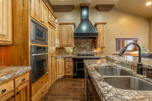 Kitchen featuring sink, dark wood-type flooring, vaulted ceiling, custom range hood, and appliances with stainless steel finishes