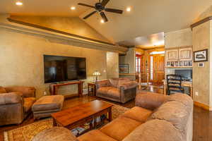 Living room with hardwood / wood-style flooring, vaulted ceiling, ceiling fan, and ornamental molding