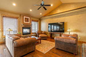 Living room featuring ceiling fan, a stone fireplace, dark hardwood / wood-style flooring, and lofted ceiling