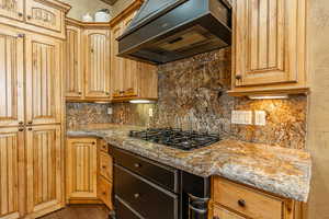 Kitchen with hardwood / wood-style flooring, decorative backsplash, light stone counters, and premium range hood