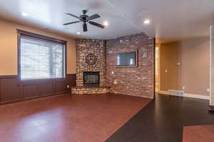 Unfurnished living room featuring a fireplace, a textured ceiling, ceiling fan, and brick wall