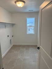 Clothes washing area featuring light tile patterned floors, washer hookup, a textured ceiling, and hookup for an electric dryer