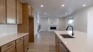 Kitchen with sink, backsplash, light brown cabinetry, stainless steel dishwasher, and light wood-type flooring