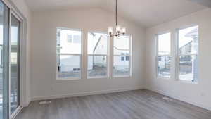 Unfurnished dining area featuring lofted ceiling, light hardwood / wood-style floors, and a chandelier