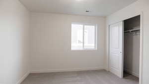 Unfurnished bedroom with light carpet and a closet