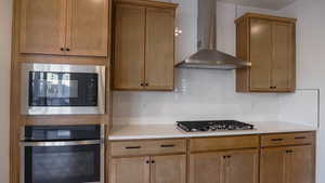 Kitchen with backsplash, appliances with stainless steel finishes, and wall chimney range hood