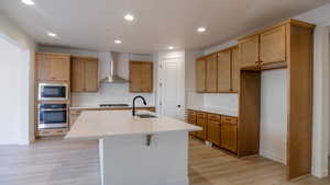 Kitchen with built in microwave, sink, oven, wall chimney range hood, and a center island with sink