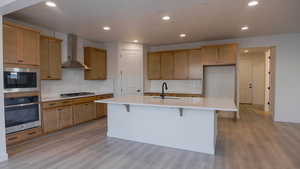 Kitchen featuring appliances with stainless steel finishes, sink, a kitchen bar, wall chimney range hood, and a center island with sink