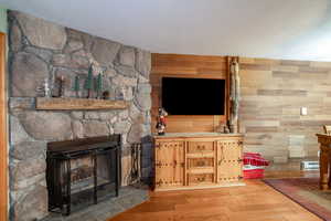 Living room with a stone fireplace, wood walls, and light hardwood / wood-style floors