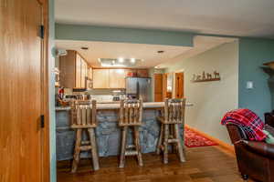 Kitchen featuring a kitchen bar, kitchen peninsula, wood-type flooring, and appliances with stainless steel finishes