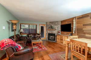 Living room with hardwood / wood-style flooring, wood walls, and a stone fireplace