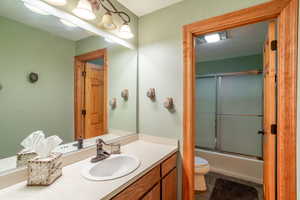 Full bathroom with combined bath / shower with glass door, vanity, tile patterned flooring, and toilet