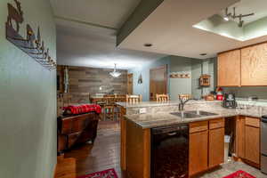 Kitchen with sink, hanging light fixtures, black dishwasher, dark hardwood / wood-style floors, and kitchen peninsula