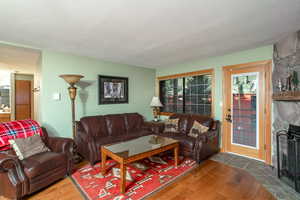 Living room with a textured ceiling, a stone fireplace, and dark wood-type flooring