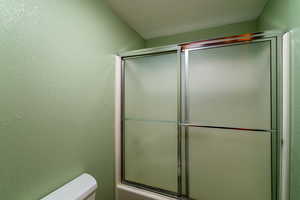 Bathroom with a textured ceiling, toilet, and bath / shower combo with glass door