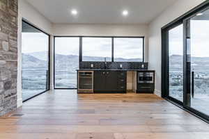 Webar with a drink cooler, dark cabinets, light wood-style floors, light stone counters, and recessed lighting