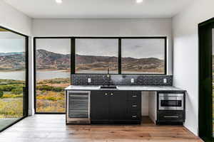 Webar with a drink cooler, dark cabinets, light wood-style floors, light stone counters, and recessed lighting