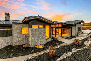 Front entry of house at dusk with a standing seam roof, a metal roof, and stone siding