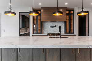 Kitchen featuring decorative backsplash, pendant lighting, light stone countertops, recessed lighting, and glass insert cabinets