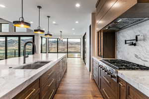 Kitchen with pendant lighting, appliances with stainless steel finishes, light wood finished floors, recessed lighting, and custom exhaust hood