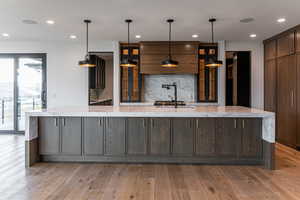 Kitchen featuring backsplash, light stone countertops, light wood finished floors, recessed lighting, and decorative light fixtures