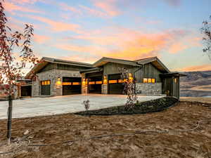 View of front of home with stone siding, driveway, board and batten siding, and an attached 3 car garage