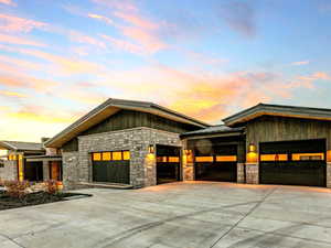 View of front of property featuring stone siding, driveway, a standing seam roof, a garage, and a metal roof