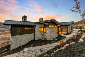 Back of house at dusk with a standing seam roof, a metal roof, and stone siding