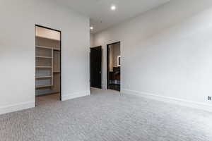 Unfurnished bedroom with a walk in closet, light carpet, and recessed lighting
