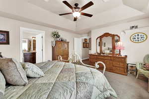 Carpeted bedroom featuring a tray ceiling, ceiling fan, and ensuite bathroom