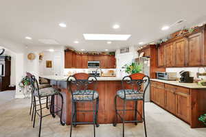 Kitchen featuring a kitchen breakfast bar, light stone counters, a center island with sink, and appliances with stainless steel finishes